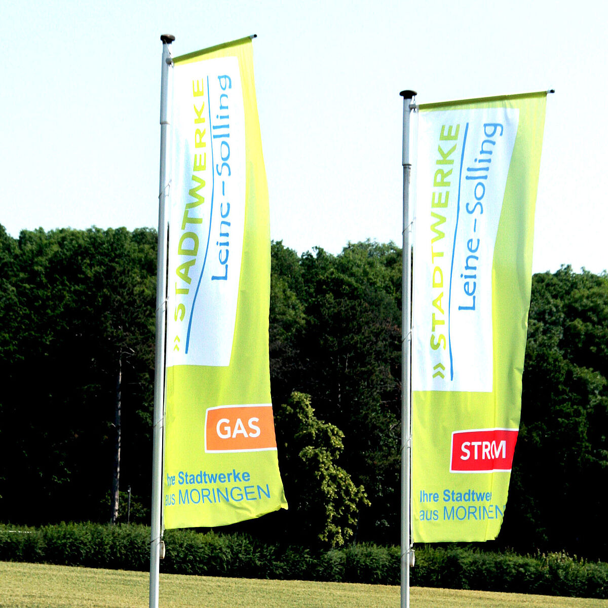 Drei Fahnen mit dem Schriftzug Stadtwerke Leine-Solling. Ihre Stadtwerke aus Moringen.Die Fahnen sind grün hinterlegt und für die Bereiche Wasser, Gas, Strom. Im Hintergrund befindet sich ein Waldrand.